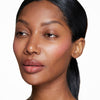 Woman with smooth, glowing skin highlighted by natural makeup, featuring subtle blush and a neutral lip color. Hair is sleekly styled back, emphasizing a fresh, polished look.