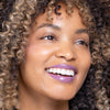 Smiling person with curly hair wearing vibrant purple lipstick.
