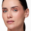 Woman with smooth skin and natural makeup, featuring soft pink eyeshadow and nude lips, against a white background.