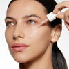 A person applying serum with a dropper onto their cheek, showcasing smooth, hydrated skin.