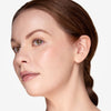 Side profile of a person with glowing, smooth skin, showcasing natural makeup with subtle blush and glossy nude lips, hair pulled back neatly.