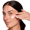 Woman applying a light pink cream to her cheek, showcasing skincare application.