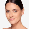 Smiling woman with clear, radiant skin, natural makeup, and neatly styled dark hair against a plain background.