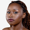Person with smooth, glowing skin and styled braided hair, showcasing a sophisticated makeup look with glossy maroon lips and enhanced eyelashes against a plain background.