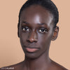 A model with a smooth complexion wears a natural makeup look, showcasing a subtle nude lip color against a neutral background.