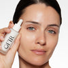 Model holding a skincare serum bottle near her face, showcasing a fresh and clear complexion.