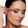 Model applying eyeshadow with a feathery brush, showcasing a gently blend shadow brush for the eyelid crease