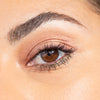 Close-up of a woman's eye showcasing expertly applied shimmery eyeshadow and defined lashes, highlighting flawless eyebrow grooming.