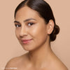 A woman with smooth, glowing skin and a subtle, natural makeup look, set against a soft beige background.