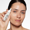 Model holding an OFIR Face Milk dropper bottle beside her cheek, showcasing a dewy, hydrated complexion