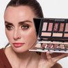 Woman showcasing an eyeshadow palette with multiple shades, highlighting a glamorous eye makeup look.