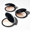 Open compacts of dual-tone powder makeup are displayed on a light background