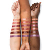 Three forearms showcasing a range of lipstick swatches in shades labeled What-Eh-Ver!, Pink Smoothie, Berry, Off Pink, All That, and Go There! against diverse skin tones.