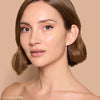 Woman with smooth, glowing skin and short brown hair showcases a natural makeup look with nude lipstick and subtle eyeliner, set against a neutral background.