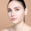 A person with flawless skin and subtle makeup, featuring neutral tones, gazes confidently against a soft beige background. Perfect for showcasing the "Bare Rice" beauty product.