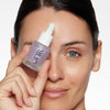 Woman holding a dropper bottle of OFIR serum close to her face, showcasing smooth, radiant skin.