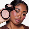 Model holding a compact powder featuring a dual-tone bronzer, highlighting contour on her cheek, and a flawless makeup finish.