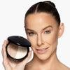 Model holding a bronzer/highlighter product to her face, showcasing a light/fair shade duo