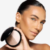 Model holding a compact powder featuring a dual-tone bronzer, highlighting contour on her cheek, and a flawless makeup finish.