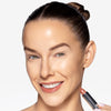 Model with glowing skin smiling and holding OFIR Lip Rouge lipstick in Off Pink shade