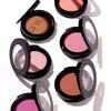 Assorted makeup compacts with shades of brown, pink, and peach in sleek black cases, designed for highlighting and contouring.