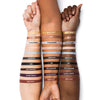 Three arms with different skin tones displaying swatches of eyeliner shades labeled Gold Dust, 6PM, Chalkshine, Nudesicle, Cloudless, Graphite, Ink, Rich Brown, Ultra Violet, and Red Clay
