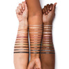 Three arms displaying a diverse range of eyeshadow shades swatched on the skin, labeled from Limestone to Basalt, highlighting color and texture variety across different skin tones.