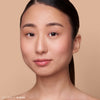 Person with smooth, radiant skin wearing subtle makeup, within a neutral-toned background.