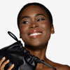  model holding an OFIR black leather drawstring pouch, wearing a warm brown glossy lip.
