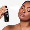 Woman with closed eyes applies facial mist from a black bottle labeled "OFIR," enhancing her glowing makeup look.