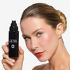Model with glowing skin holding OFIR Ever Set setting spray black pump bottle