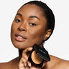 Model holding a compact setting powder, showcasing a tan shade and a flawless makeup finish.