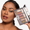 Model showcasing a glam makeup look focused on a gold and brown eyeshadow while holding the perennial next to her face 
