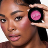 A model showcasing OFIR blush, highlighting rosy cheeks and a natural makeup look. The blush compact is held near the face, emphasizing its vibrant pink shade.