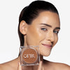 Model holding a compact bronzer while showcasing a light/brownish nude shade on her cheekbones and a flawless makeup finish.