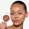 Model holding a compact bronzer while showcasing a medium dark nude shade on her cheekbones and a flawless makeup finish.