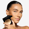 Model holding a compact setting powder, showcasing a light shade and a flawless makeup finish.