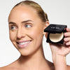 Model holding a compact setting powder, showcasing a vary light/fair shade and a flawless makeup finish.