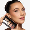 model with a warm bronze eye look holding an open OFIR Simple Six eyeshadow palette beside her face