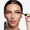 Model holding a mascara to her eyelashes, showcasing a black and smooth finish