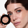 Woman showcasing a compact powder with a radiant finish, held near her face, highlighting smooth skin and neutral makeup tones.