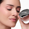 Woman showcasing a compact labeled "OFIR," highlighting smooth, radiant skin and subtle pink makeup tones.