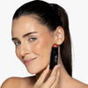 Model holding near her cheek  a deep berry blush stick in a black tube, showcasing a purplish blush pigmentation in a radiant natural look