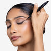 Model holding a liquid eye liner to her eyes, showcasing a deep brown, sharp, and smooth line