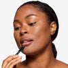 Model holding a lip liner to her mouth, showcasing a brown shade