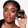 Model holding a shadow palette in one hand, with the shades applied to her eyes, showcasing an earthy tones makeup look