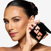 Model holding a shadow palette in one hand, with the shades applied to her eyes, showcasing an orange-ish makeup look