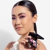 Model holding a shadow palette in one hand, with the shades applied to her eyes, showcasing a mauve makeup look