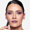 Model holding a mauve lipstick in one hand, with the shade applied to her lips, showcasing a mauve makeup look