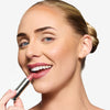 Model holding a berry pink lipstick in one hand, with the shade applied to her lips, showcasing a pink makeup look